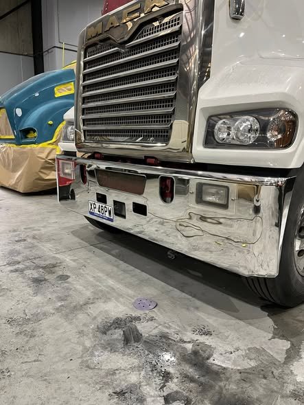 Close-up of a polished Mack bumper reflecting the workshop floor