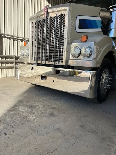 Polished Kenworth bumper and grille shining under shed lights
